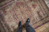 Antique Kerman rug detail showing intricate ivory, cochineal red, navy blue floral motifs and visible wear.