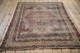 Corner of antique Kerman rug, showcasing scrolling floral borders and tattered fringe.