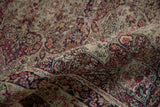Faded scrolling arabesque and floral motifs on antique Kerman rug with wear in red, ivory, navy.