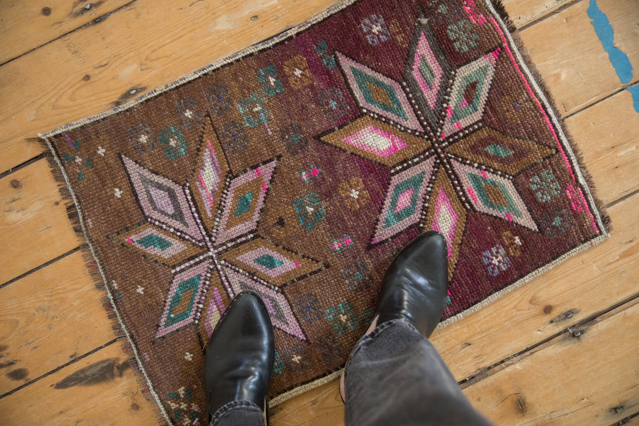 Distressed Kars rug with abrashed aubergine field, faded magenta starburst, and floral motifs.
