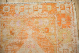 Distressed Oushak rug texture showing bright tangerine orange, ivory, and knot heads.