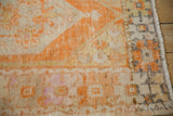 Distressed Oushak rug corner with tangerine, ivory geometric border and visible knot heads.