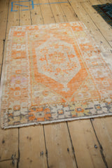 Distressed tangerine and ivory Oushak rug corner, showing geometric border, muted charcoal, and fringe.