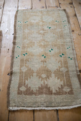 Distressed Oushak rug close-up: soft pile, ivory and pale brown serrated guls, green accents.