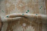 Close-up of a folded distressed Oushak rug, showing soft pile texture and subtle emerald green pops.