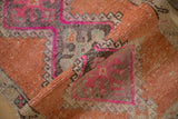 Close-up of rolled distressed Kars rug pile with geometric fuchsia and terracotta patterns.