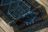 Geometric blossom motif in cobalt blue and dark ochre on a distressed Kars rug corner.