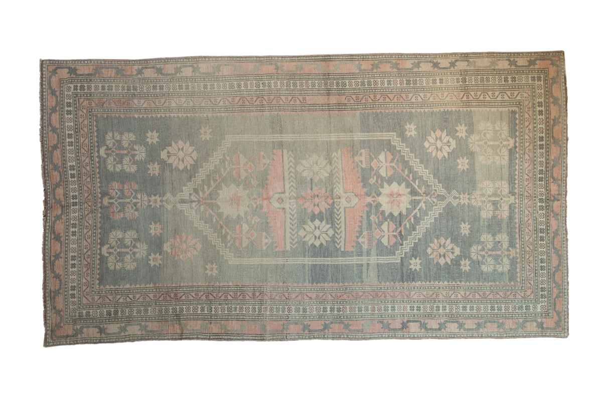 Distressed vintage Oushak carpet featuring faded blue, rose, and ivory geometric medallion, 4'10" x 8'9".
