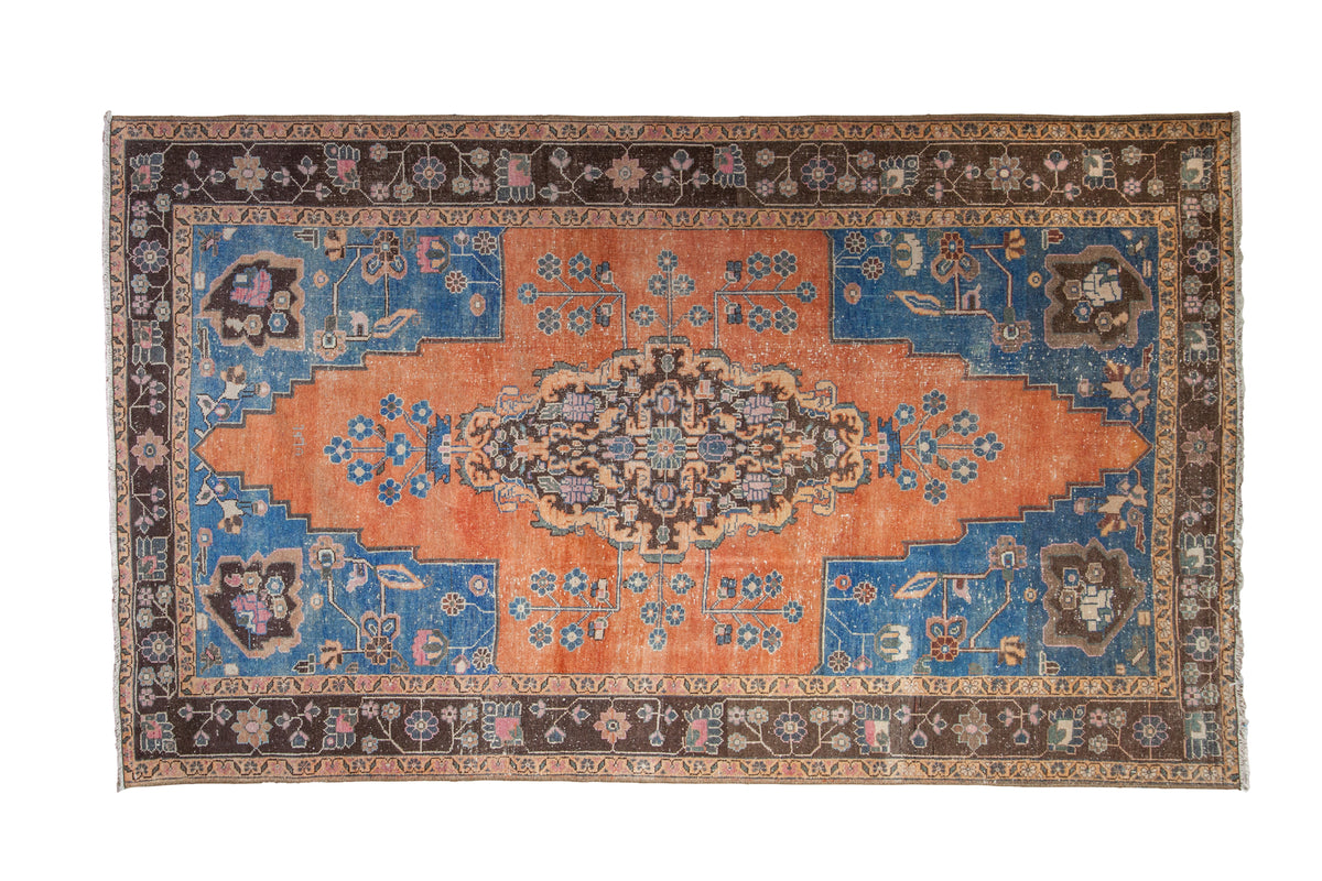 Distressed vintage Oushak rug with an elongated orange medallion, sapphire blue corners, and floral border.