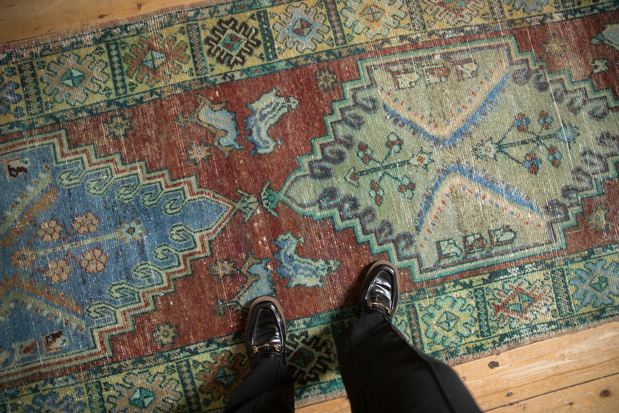 Distressed Anatolian runner showing faded geometric patterns in burgundy, blue, and green, with worn pile.