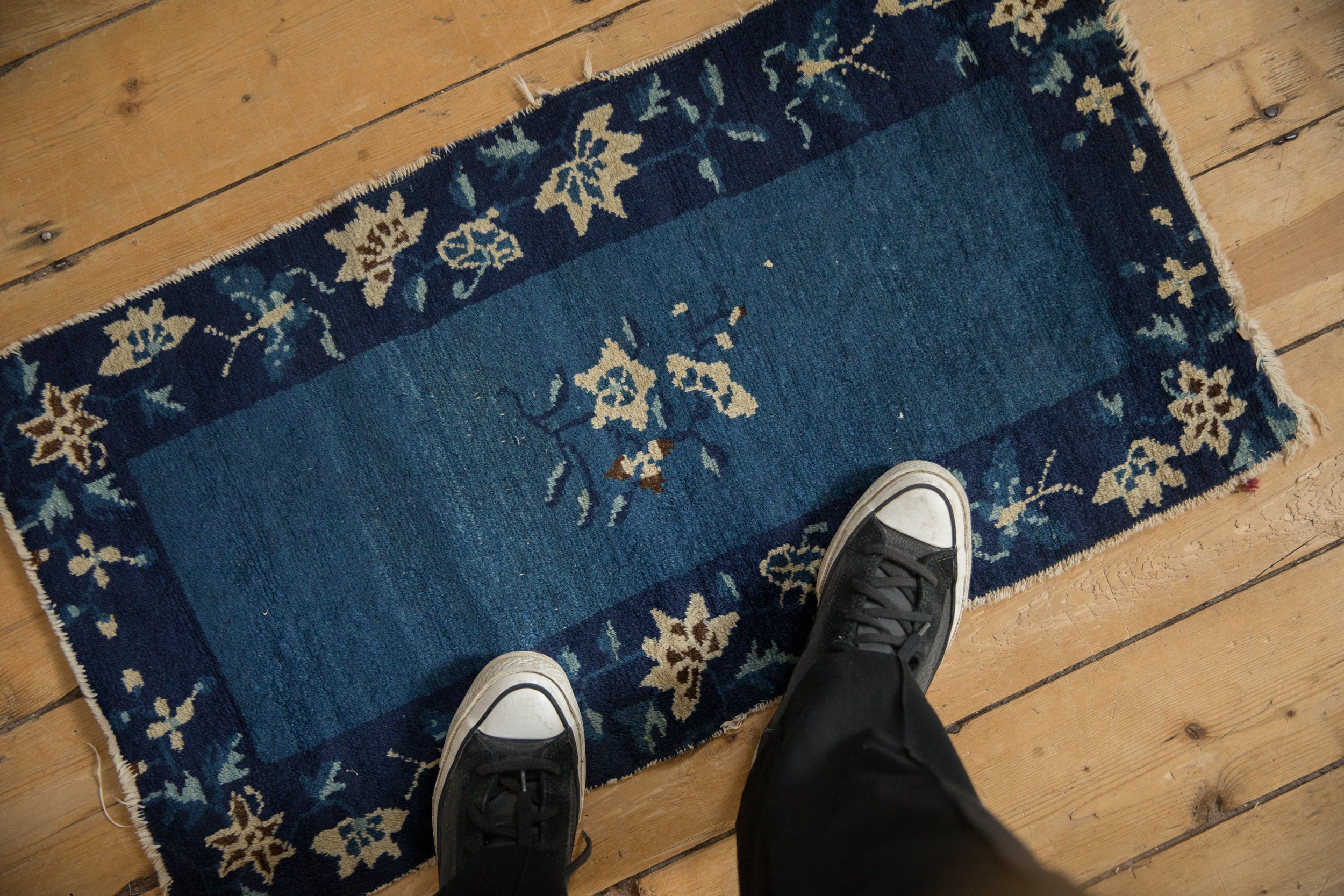Peking rug close-up: navy border with ivory lotus and butterfly design, visible wear.
