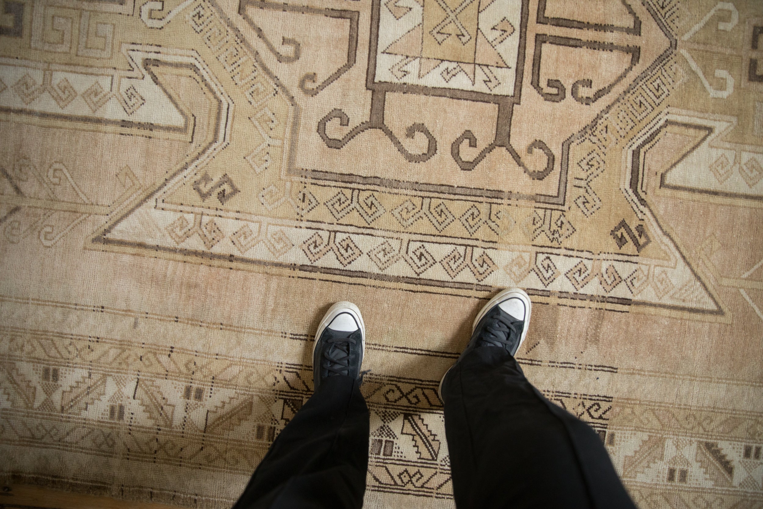 Worn texture and geometric patterns of a vintage Kars carpet in neutral beige tones.
