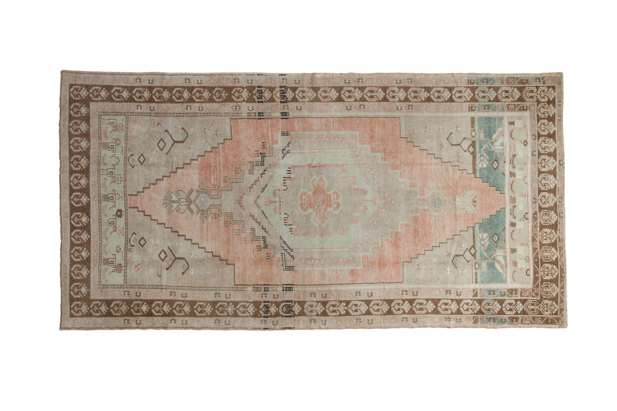 Distressed vintage Oushak rug features a muted peach, grey, and teal geometric medallion.