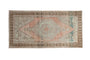 Distressed vintage Oushak rug features a muted peach, grey, and teal geometric medallion.