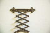 Antique mirror's accordion mechanism and fleur de lis hardware with darkened patina.