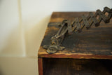 Fleur de lis hardware and accordion mechanism of antique shaving mirror with darkened patina.