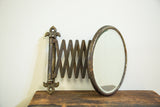 Antique round beveled glass mirror with darkened metal accordion mount and fleur de lis.