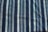 Close-up of hand-woven indigo textile with intricate striped pattern and natural dye variations.