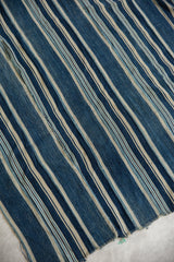 Hand-woven African indigo textile, varied blue and cream stripes, showing texture and wear.
