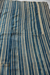 Hand woven African indigo textile with varied blue and natural striped pattern, featuring pieced seams.
