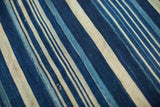 Vintage hand-dyed indigo textile with varied blue stripes and cotton weave.