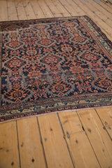 Angled view of an antique Malayer rug showing its energized allover tribal pattern on a navy blue field.