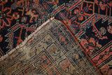 The hand-knotted foundation and wool pile of an antique Malayer rug revealed at the corner.