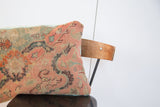 Intricate peach, muted blue, and green floral pattern on antique Turkish rug fragment pillow with light blue piping.