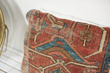 Hand-knotted Heriz rug fragment pillow with geometric patterns in rich terracotta and blue.