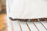 Worn Heriz rug fragment edge in rust, teal, beige next to the linen pillow back.