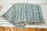 Hand woven indigo textile displaying light blue and ivory patterned stripes and fringe.