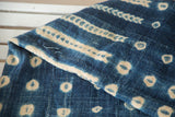 Folded African indigo textile with distinctive ivory patterns and visible hand-woven texture.