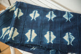 Folded vintage African indigo textile, revealing unique ivory patterns and hand-woven texture.