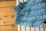 Hand-woven African indigo textile detail with ivory pattern, stitched design, and short tassels.
