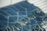 Textured vintage African indigo textile, revealing geometric pattern and frayed fringe.