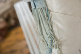 Close-up of sun-faded indigo pillow tassels and ivory European linen back with enclosure detail.
