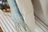Sun-faded indigo textile, long tassels, and textured ivory linen pillow back.