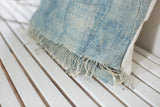 Sun-faded light blue indigo pillow, detailed view of short ivory tassels.
