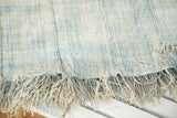 Frayed fringe and textured surface of a hand-woven African indigo textile in faded blues.