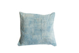 Sun-faded light blue indigo textile pillow texture with subtle vertical stripe pattern.
