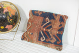 Antique Kazak rug pillow close-up, revealing worn geometric pattern and faded turquoise linen back.