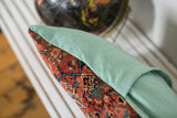 Red and blue Herati pattern on antique Bijar rug fragment beside sea foam linen.