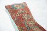 Detail of Heriz pillow's worn red, blue, and beige rug fragment with sea foam linen back.