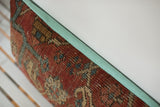 Aged red Heriz rug fragment pillow with geometric pattern and sea foam green linen edge.