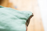 Sea foam green linen pillow back, white stitching, and vintage Heriz rug edge.