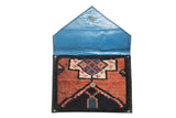 Open clutch reveals geometric Oushak rug pattern, bright blue leather lining, and metal snap.