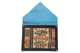 Rug fragment clutch opened to show its bright blue vegetable suede lining and metal snap.