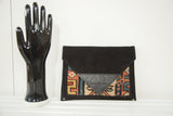 Side angle of the handmade clutch showing its black suede body and corner rivet detail.