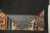 Close-up of the embossed leather Swag and Tassel logo on the suede and antique rug clutch.