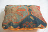Textured antique Caucasian rug fragment pillow with natural wear and geometric blue, orange patterns.